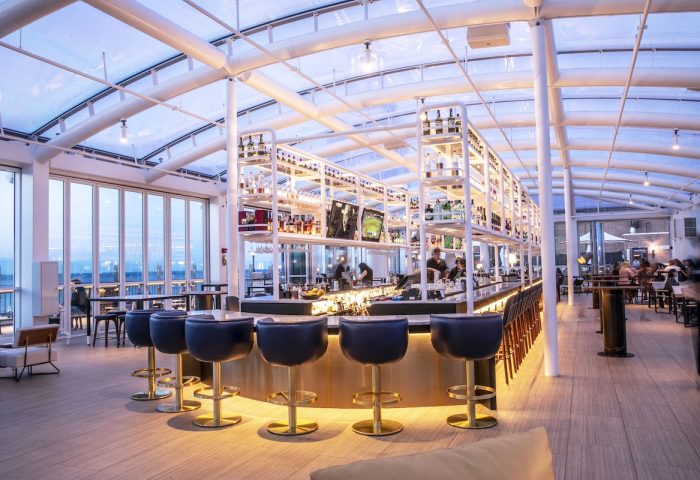 Interior of Sable at Navy Pier Chicago, a gay-friendly Curio Collection by Hilton hotel. Bar with stools, bottles, and a transparent roof.