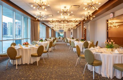 Sable at Navy Pier Chicago, Curio Collection by Hilton ballroom. Tables with white tablecloths, chairs, and centerpieces. Chandelier lighting.