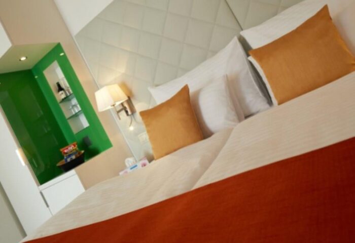 Safestay Vienna gay-friendly hotel room. Modern design with orange accents, white bedding, and a green niche with snacks and drinks.