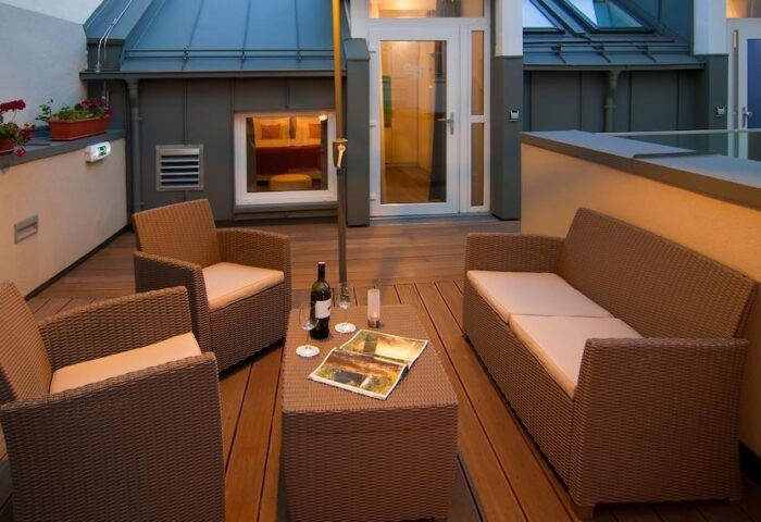 Safestay Vienna gay-friendly hotel patio. Outdoor seating with wicker chairs, sofa, table, wine, and a magazine. Relaxing travel for gay men.