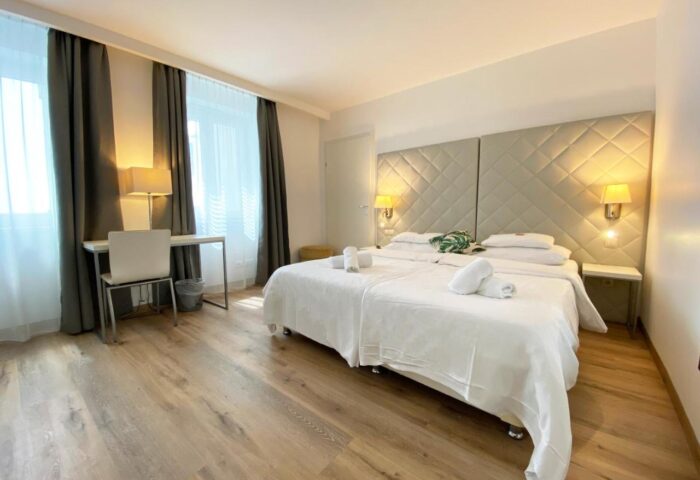 Safestay Vienna gay-friendly hotel room. Double bed with white linens, desk, and lamps. Modern, clean design. Ideal for gay travelers.