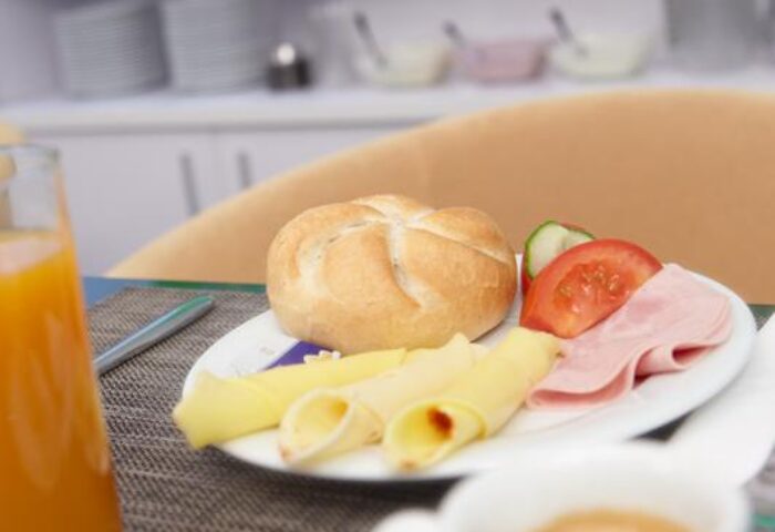 Breakfast at Gay-Friendly Hotel Safestay Vienna. Roll, cheese, ham, tomato, cucumber, orange juice, and coffee on a plate. Vienna hotel food.