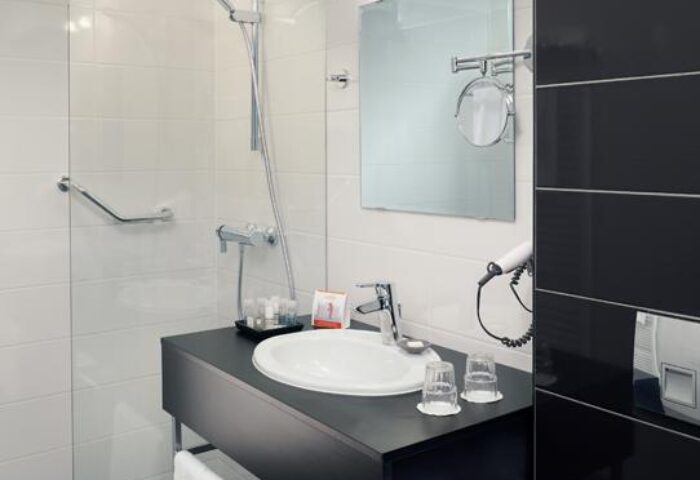 Safestay Vienna's gay-friendly hotel bathroom. Modern design with white tiles, shower, sink, and mirror. Ideal for gay men travelers.