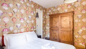 Salotto Monti gay-friendly hotel room. Bedroom with hot air balloon wallpaper, wooden wardrobe, and white linens. Gay travel in Rome.