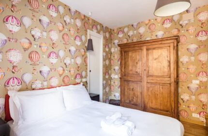 Salotto Monti gay-friendly hotel room. Bedroom with hot air balloon wallpaper, wooden wardrobe, and white linens. Gay travel in Rome.