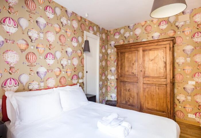 Salotto Monti gay-friendly hotel room. Bedroom with hot air balloon wallpaper, wooden wardrobe, and white linens. Gay travel in Rome.