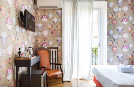 Salotto Monti gay-friendly hotel room. Hot air balloon wallpaper, leather chair, and bright window. LGBTQ+ travel in Rome, Italy.