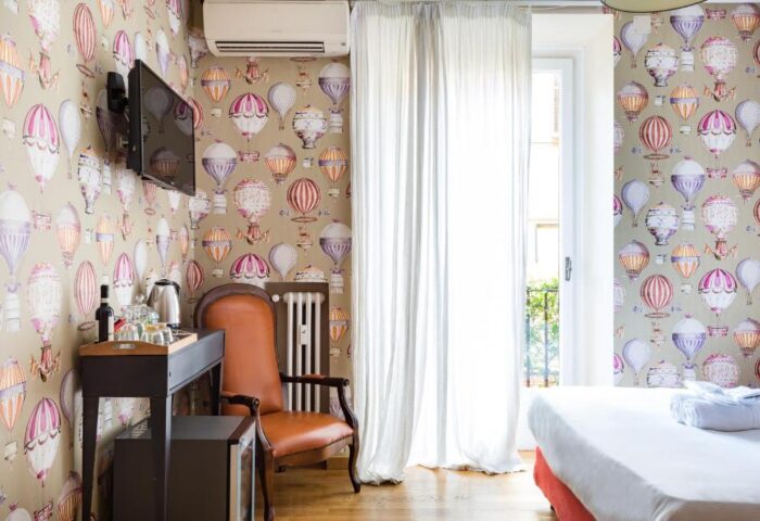 Salotto Monti gay-friendly hotel room. Hot air balloon wallpaper, leather chair, and bright window. LGBTQ+ travel in Rome, Italy.