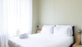 Bedroom at Gay-Friendly Hotel Salotto Monti. Double bed with white linens, bedside tables, lamps, and white curtains. Cozy gay travel lodging.