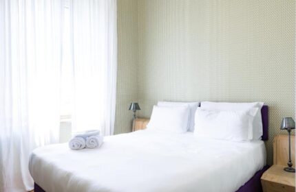 Bedroom at Gay-Friendly Hotel Salotto Monti. Double bed with white linens, bedside tables, lamps, and white curtains. Cozy gay travel lodging.