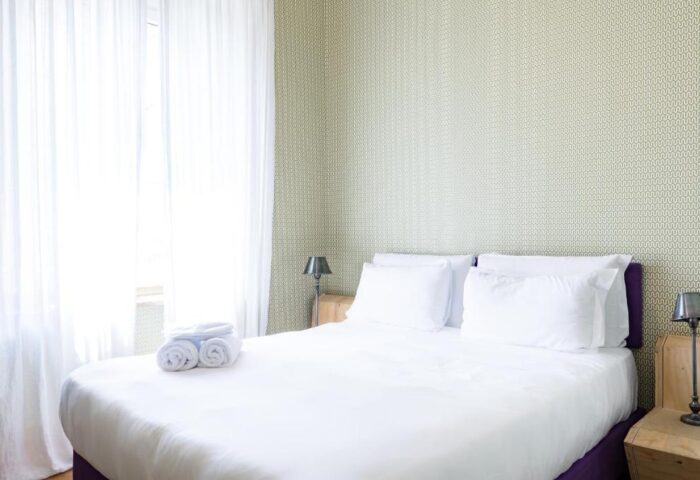 Bedroom at Gay-Friendly Hotel Salotto Monti. Double bed with white linens, bedside tables, lamps, and white curtains. Cozy gay travel lodging.
