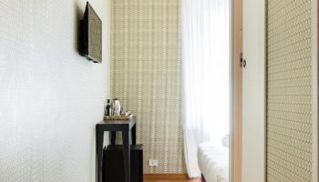 Salotto Monti gay-friendly hotel room. View of bed, herringbone wood floor, patterned wallpaper, TV, small table, and mini fridge.