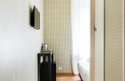 Salotto Monti gay-friendly hotel room. View of bed, herringbone wood floor, patterned wallpaper, TV, small table, and mini fridge.