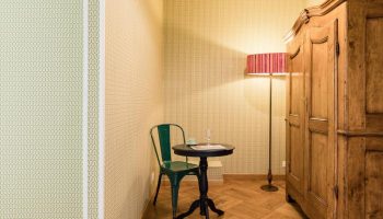 Salotto Monti gay-friendly hotel room. Green chair at small round table, floor lamp, and wooden armoire. Parquet floor. Wallpapered walls.