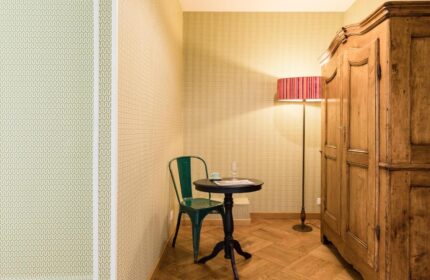 Salotto Monti gay-friendly hotel room. Green chair at small round table, floor lamp, and wooden armoire. Parquet floor. Wallpapered walls.