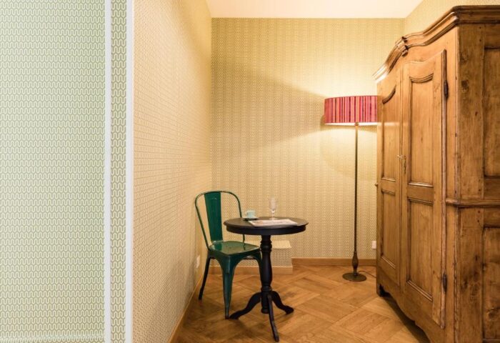 Salotto Monti gay-friendly hotel room. Green chair at small round table, floor lamp, and wooden armoire. Parquet floor. Wallpapered walls.