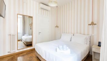Salotto Monti gay-friendly hotel room. Bedroom with double bed, striped wallpaper, mirror, and bedside table. Modern, clean design.