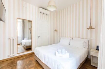 Salotto Monti gay-friendly hotel room. Bedroom with double bed, striped wallpaper, mirror, and bedside table. Modern, clean design.