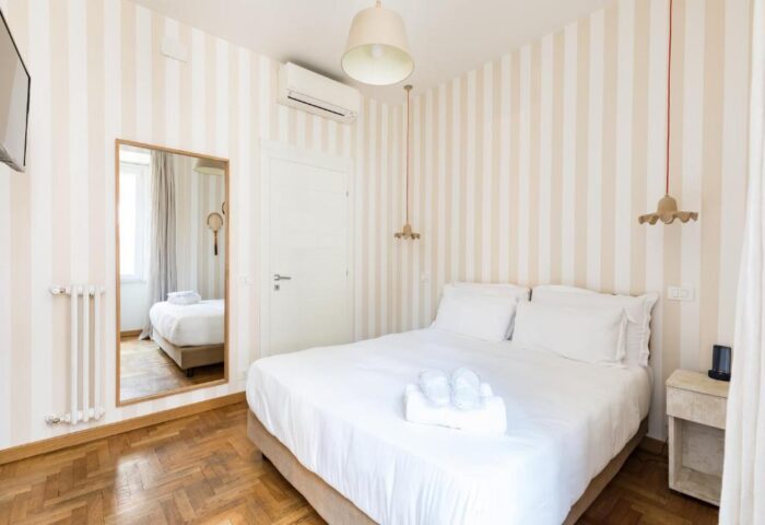 Salotto Monti gay-friendly hotel room. Bedroom with double bed, striped wallpaper, mirror, and bedside table. Modern, clean design.