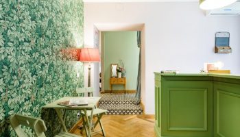 Salotto Monti's gay-friendly hotel lobby. Green leaf wallpaper, a table with chairs, and a green reception desk create a welcoming space.