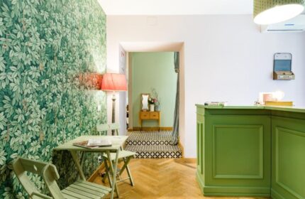 Salotto Monti's gay-friendly hotel lobby. Green leaf wallpaper, a table with chairs, and a green reception desk create a welcoming space.