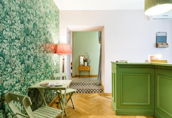 Salotto Monti's gay-friendly hotel lobby. Green leaf wallpaper, a table with chairs, and a green reception desk create a welcoming space.