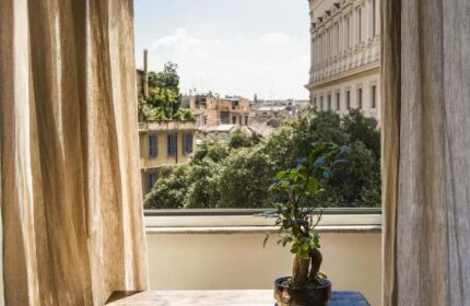 Salotto Monti gay-friendly hotel room view. Table with books and plant. Balcony overlooking Rome's cityscape. Interior design, travel advice.