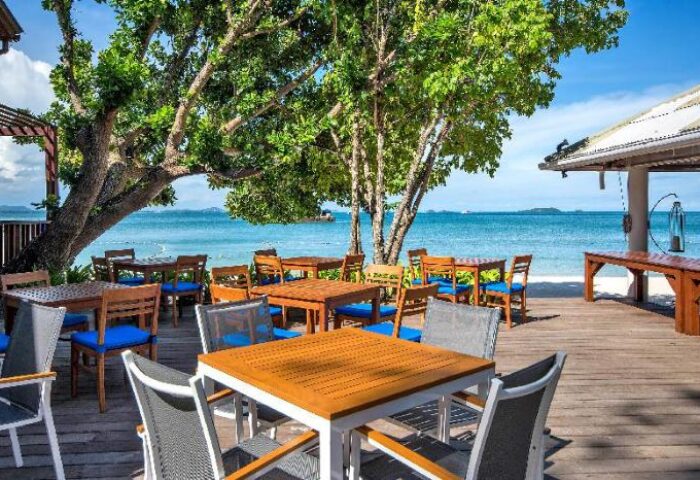 Samed Club Resort's outdoor dining area on a wooden deck, tables with blue chairs, beachfront view. Gay-friendly hotel in Thailand.