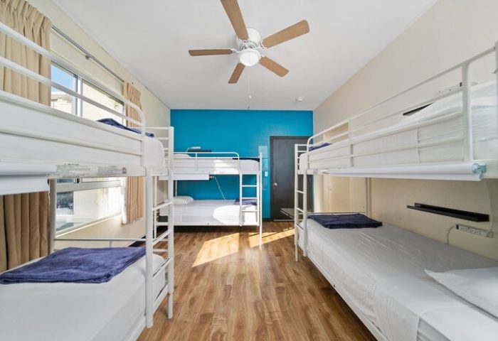 Samesun Hollywood hostel dorm room. Gay-friendly hotel near Walk of Fame with bunk beds, wood floor, blue accent wall, and ceiling fan.