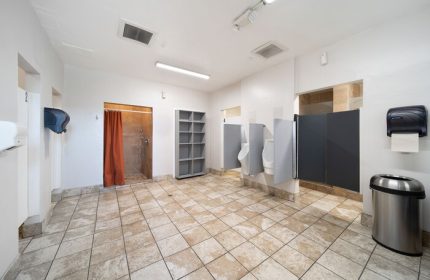 Bathroom at Samesun Hollywood (formerly Walk of Fame Hostel), a gay-friendly hotel. Features urinals, stalls, shower, and open shelving.