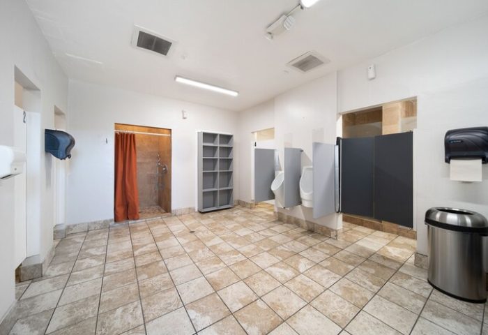 Bathroom at Samesun Hollywood (formerly Walk of Fame Hostel), a gay-friendly hotel. Features urinals, stalls, shower, and open shelving.