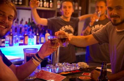 Gay-friendly Samesun Montreal Central Hotel bar scene. Men toasting drinks, celebrating. Nightlife at the central hostel.