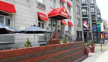 Samesun Montreal Central, a gay-friendly hotel. The building's facade has red awnings. Flags wave near this central Montreal hotel.