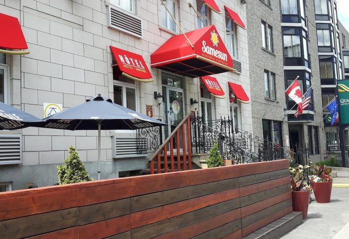 Samesun Montreal Central, a gay-friendly hotel. The building's facade has red awnings. Flags wave near this central Montreal hotel.