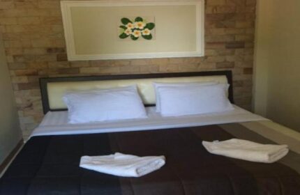 Samet Inn gay-friendly hotel room. Double bed with white linens, brown and black striped bedspread. Floral art on brick wall. Koh Samet, Thailand.