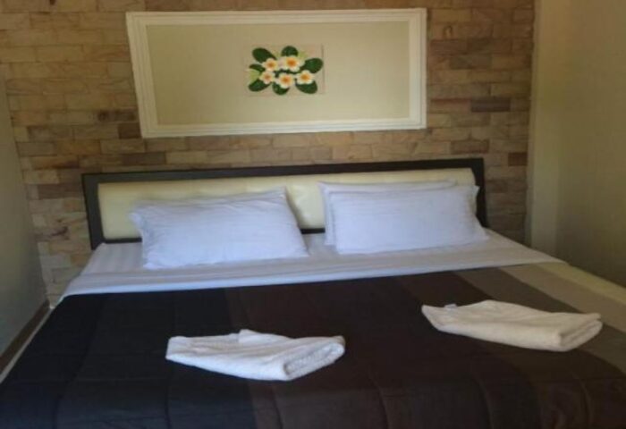 Samet Inn gay-friendly hotel room. Double bed with white linens, brown and black striped bedspread. Floral art on brick wall. Koh Samet, Thailand.