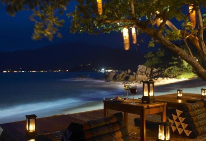 Santhiya Koh Phangan Resort & Spa gay-friendly hotel outdoor dining at night. Beachfront tables, lanterns, wine, and ocean views.