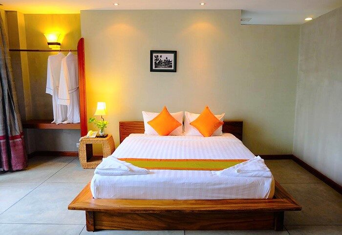 Saravoan Royal Palace bedroom. Gay-friendly hotel room with a bed, orange pillows, and robes. Ideal for gay men's travel in Cambodia.