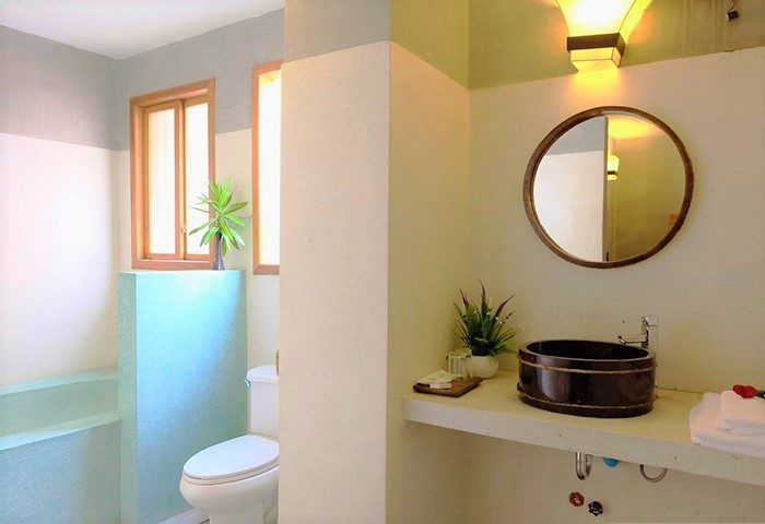 Saravoan Royal Palace gay-friendly hotel bathroom. Round mirror above a vessel sink, toilet, and natural light from windows. Clean, modern design.