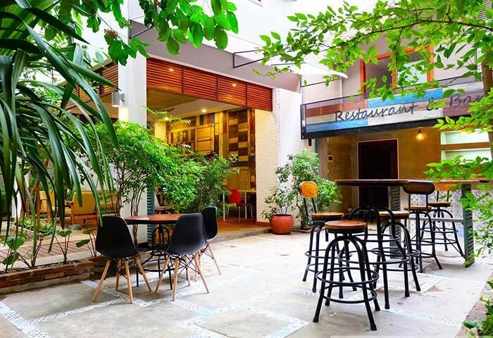 Saravoan Royal Palace's courtyard, a gay-friendly hotel. Outdoor seating area with tables, chairs, and lush greenery. Restaurant & Bar sign visible.