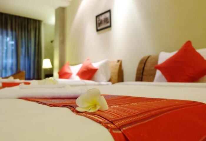 Saravoan Royal Palace gay-friendly hotel room. Beds with red accents, white flower. Gay travel lodging in Cambodia. Interior of hotel.