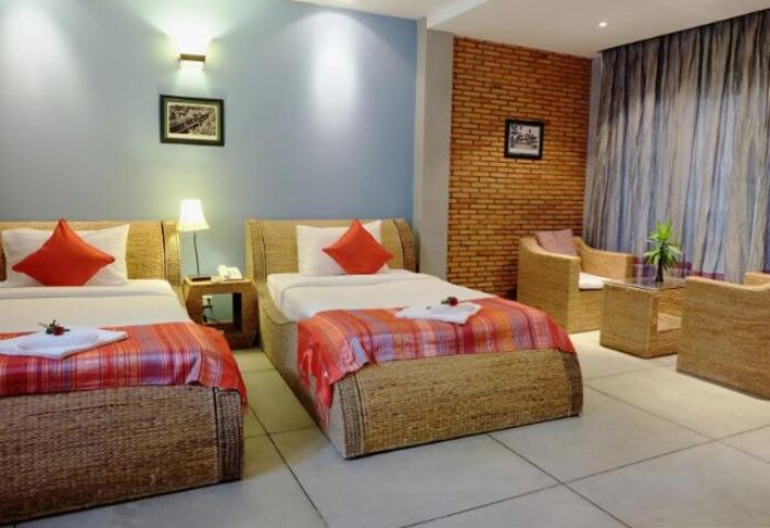 Saravoan Royal Palace gay-friendly hotel room. Two beds with red accents, wicker furniture, brick wall. Comfortable stay for gay travelers.