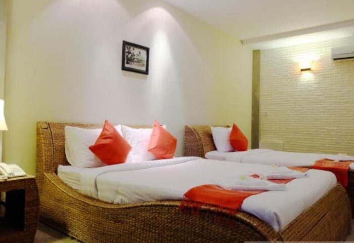 Saravoan Royal Palace room. Gay-friendly hotel with twin beds, orange accents, and woven headboards. Comfortable stay for gay travelers.