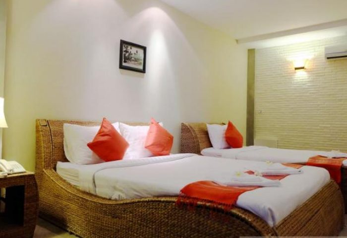 Saravoan Royal Palace room. Gay-friendly hotel with twin beds, orange accents, and woven headboards. Comfortable stay for gay travelers.