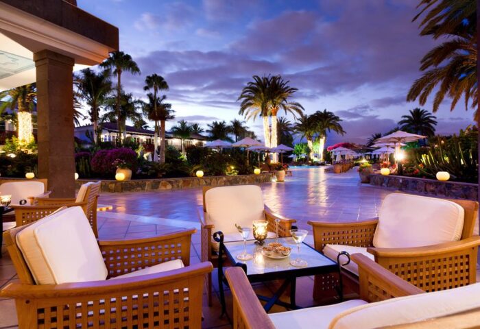 Seaside Grand Hotel Residencia Gran Lujo patio at dusk. Gay-friendly hotel with luxury outdoor seating, palm trees, and a relaxed ambiance.