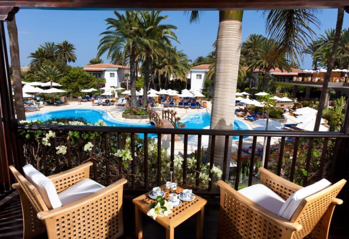 Balcony view at Seaside Grand Hotel Residencia Gran Lujo, a gay-friendly hotel. Pool, palms, and chairs offer a luxurious resort experience.