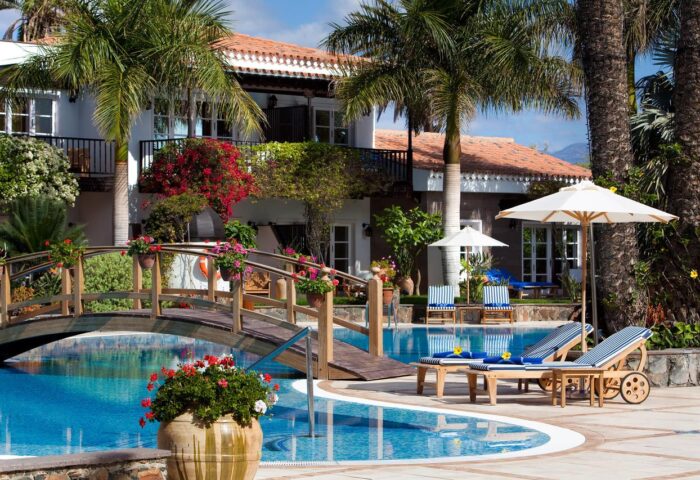 Seaside Grand Hotel Residencia Gran Lujo pool view. Gay-friendly hotel with bridge over pool, lounge chairs, and palm trees. Luxury travel.