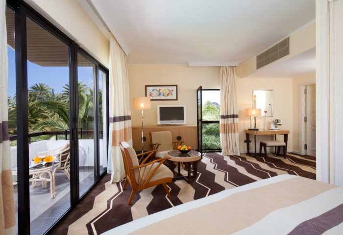 Seaside Palm Beach gay-friendly hotel room. Balcony view of palm trees, seating area, desk, and modern decor. Relaxing travel destination.