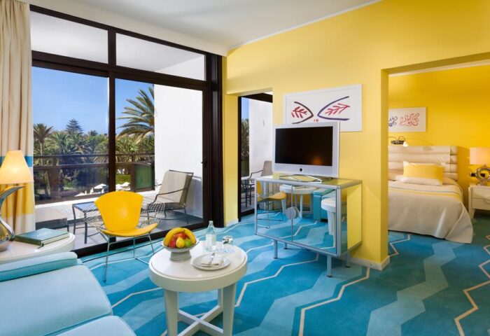 Seaside Palm Beach gay-friendly hotel room with balcony. Yellow walls, blue carpet, and modern furniture. A bright, welcoming space.