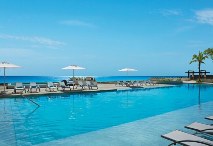Secrets The Vine Cancun Resort & Spa pool view. All-inclusive, adults-only, gay-friendly hotel. Ocean view, lounge chairs, and umbrellas.